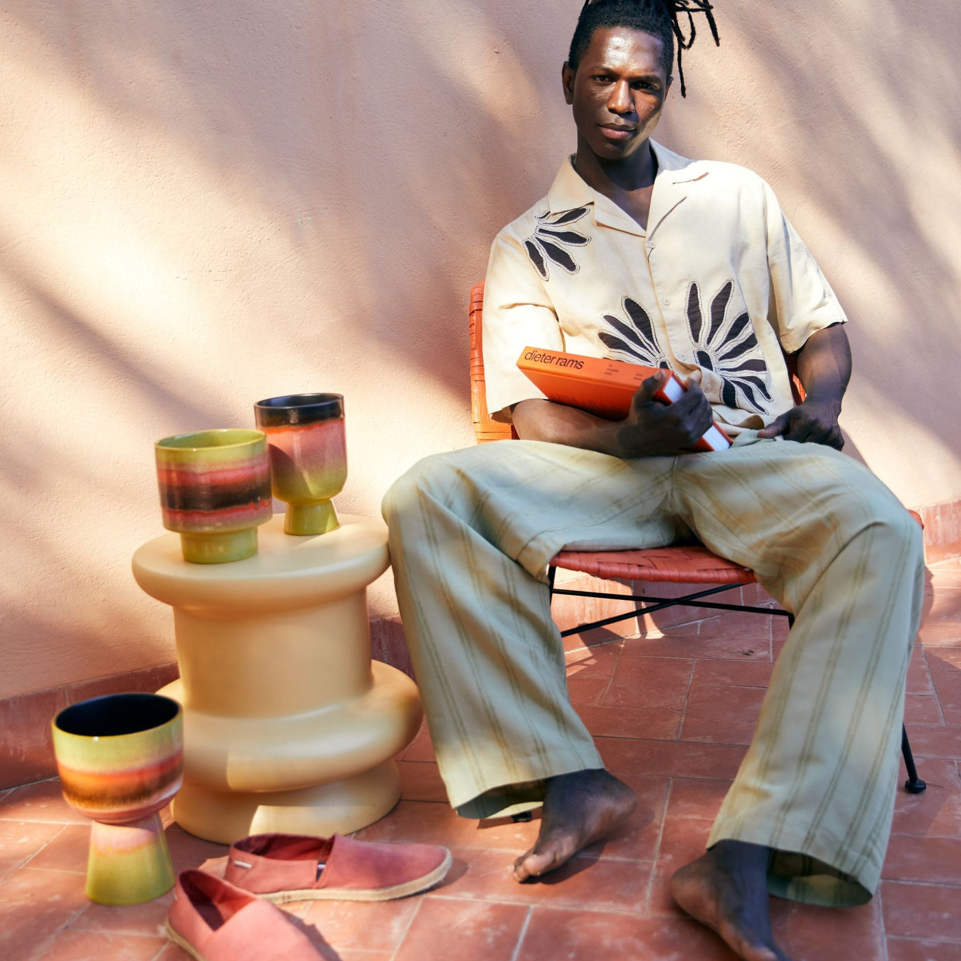 Person sitting on a chair with colorful stools and cups on a red brick floor.