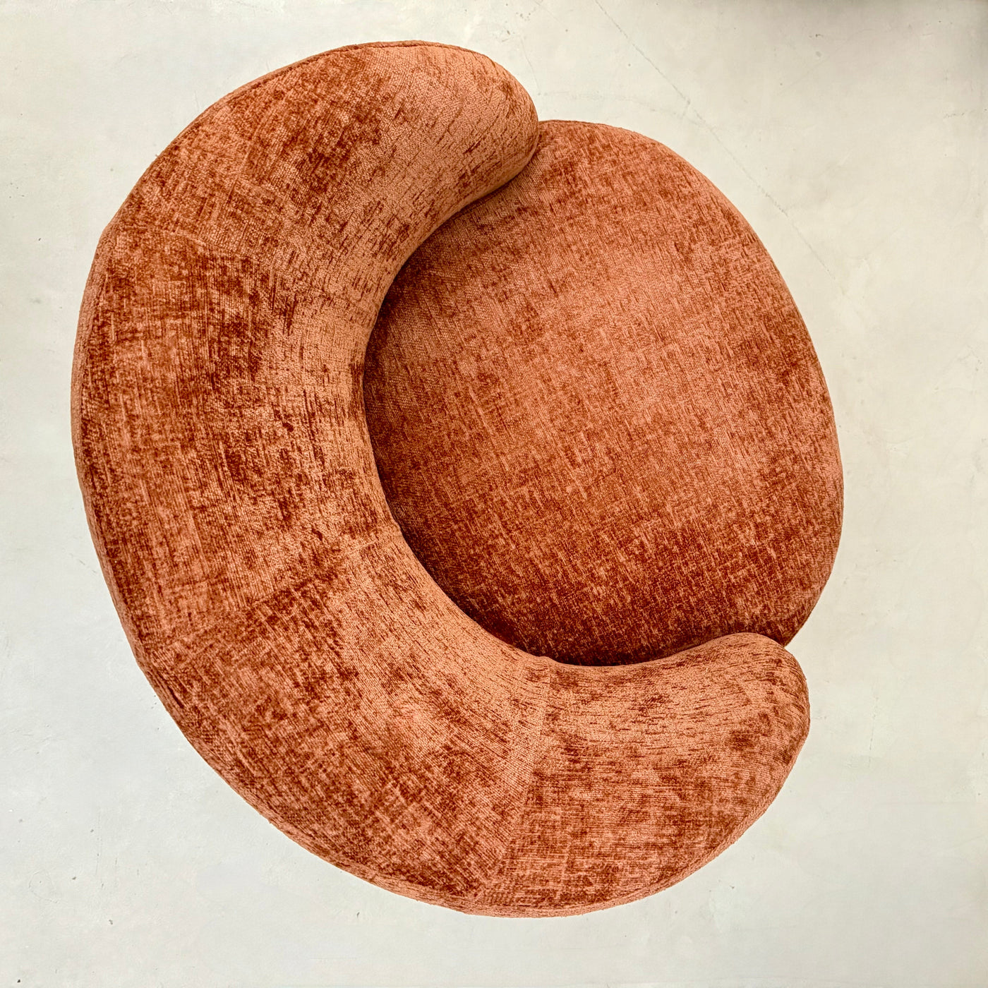 Terracotta chenille swivel armchair in a room with a wooden cabinet and plants.-Mrs Robinson