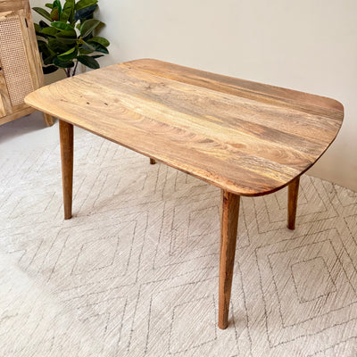 Wooden dining table on a textured floor with a plant in the background