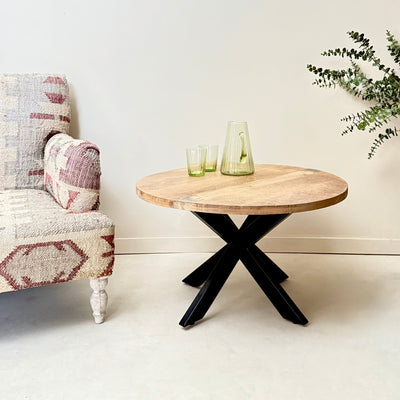Round wooden table with black metal legs next to a patterned armchair in a minimalistic room. Mrs Robinson