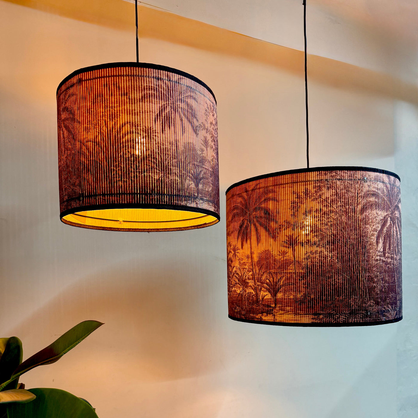 Two pendant lights with palm tree patterned shades on a neutral background