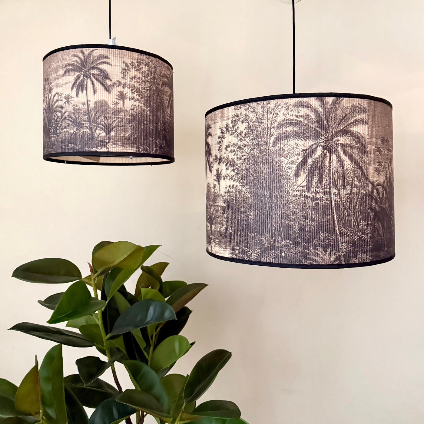 Two pendant lamps with palm tree design lampshades next to a plant on a neutral background