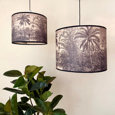 Two pendant lamps with palm tree design lampshades next to a plant on a neutral background