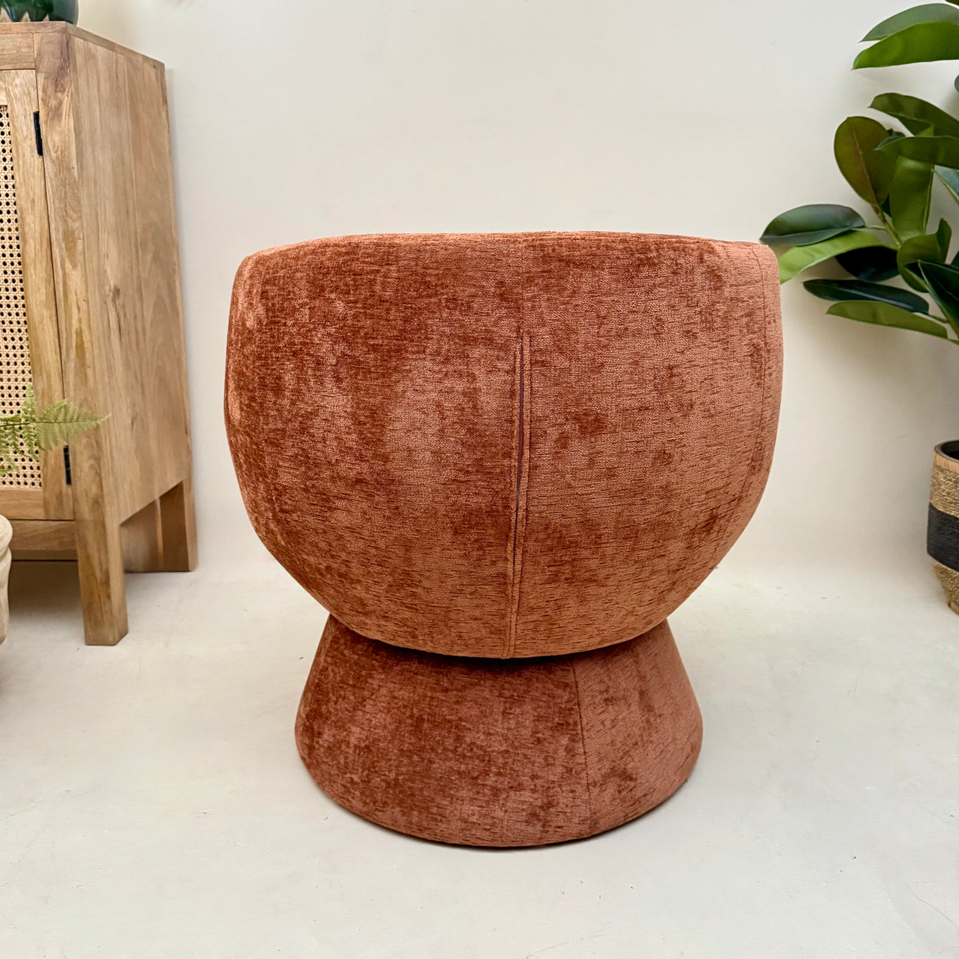 Terracotta chenille swivel armchair in a room with a wooden cabinet and plants.-Mrs Robinson