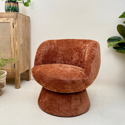 Terracotta chenille swivel armchair in a room with a wooden cabinet and plants.-Mrs Robinson