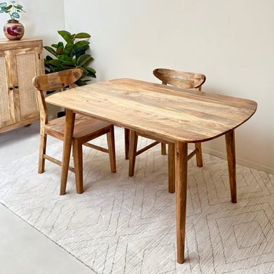 Wooden dining table with two chairs in a room with a rug and cabinet.