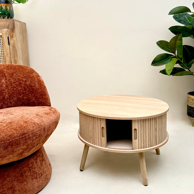 Wooden side table with a cat house design next to a brown armchair in a room with plants. Mrs Robinson