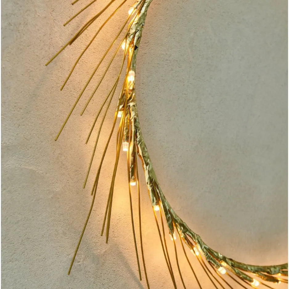 Decorative wreath with gold branches and string lights on a neutral background