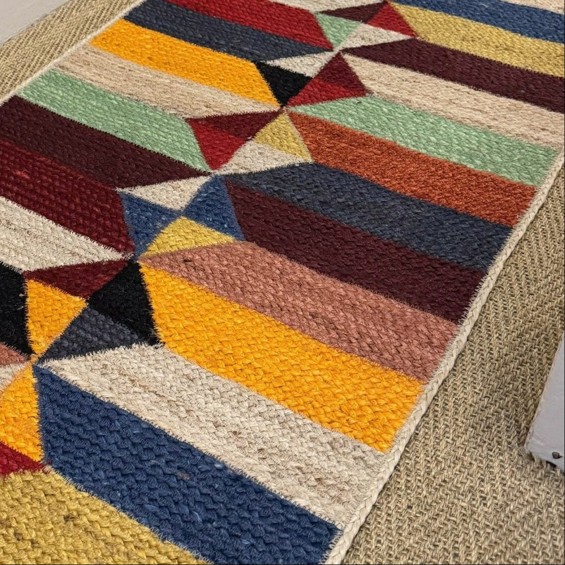 Colorful geometric-patterned rug on a carpeted floor with a neutral wall background