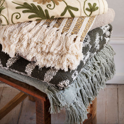 Stack of decorative blankets with floral and geometric patterns on a wooden stool.