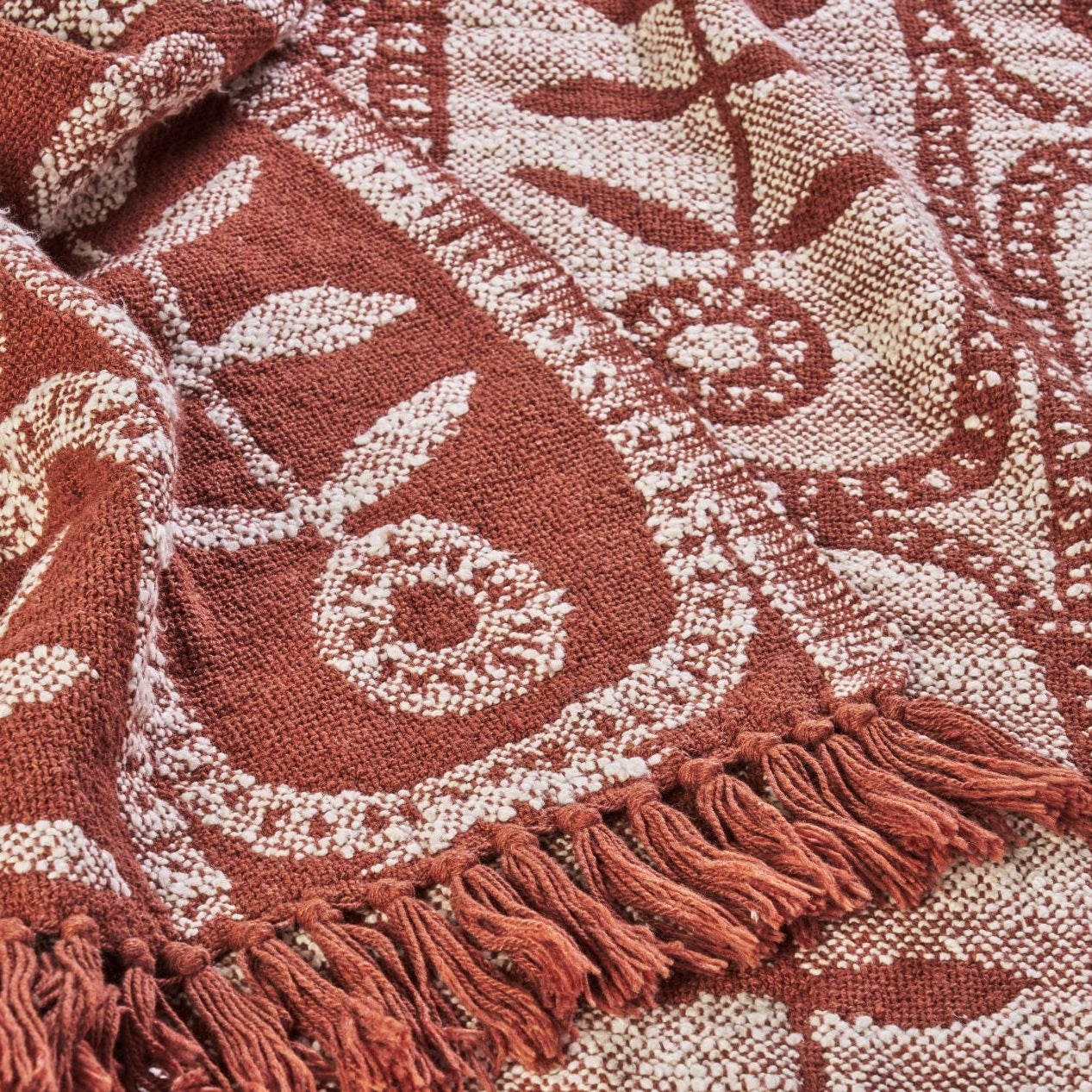 Close-up of a patterned fabric with fringes in red and beige tones.