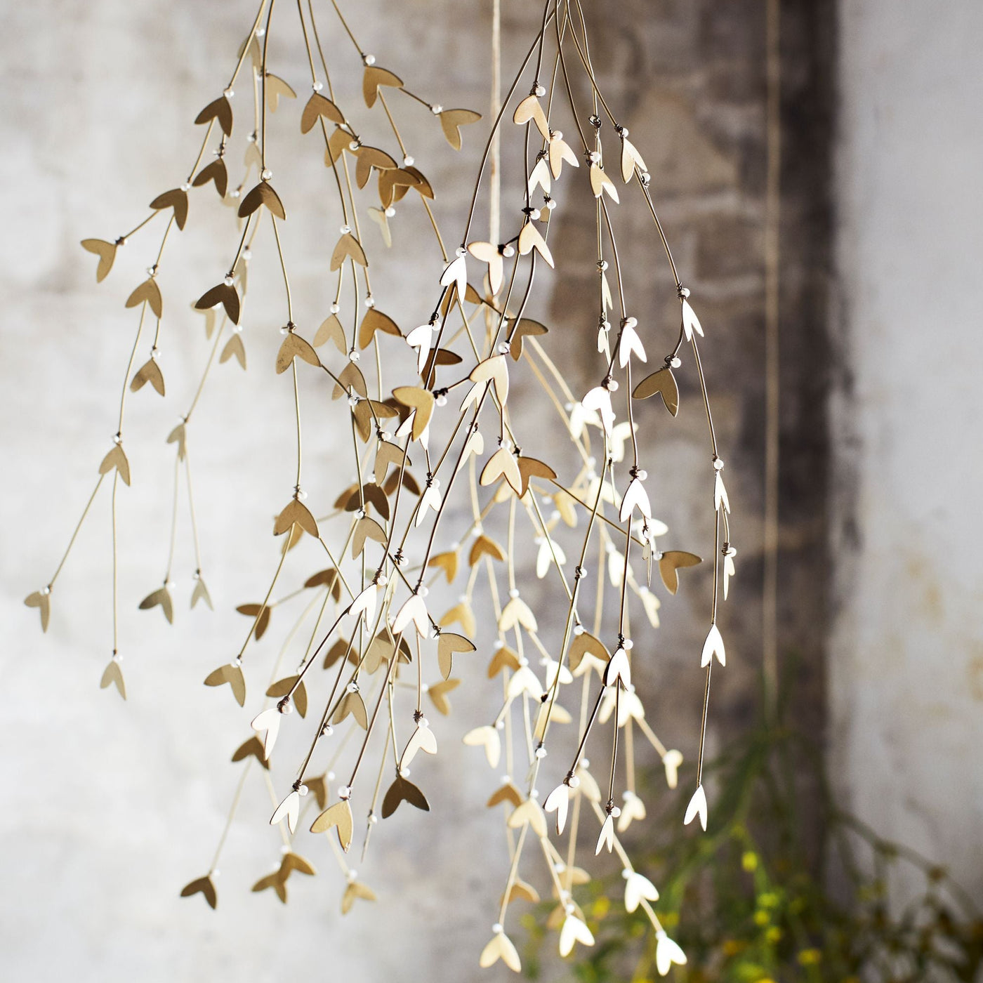 Decorative hanging misletoe with gold and white leaves against a stone wall.