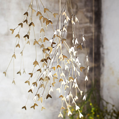 Decorative hanging misletoe with gold and white leaves against a stone wall.