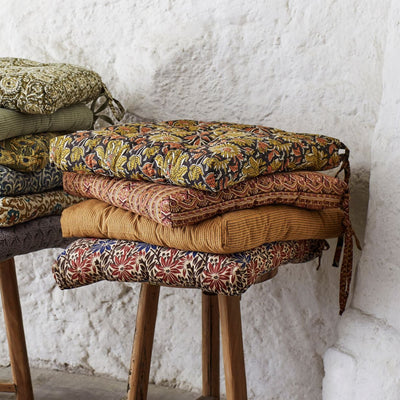 Stack of patterned cushions on a wooden stool against a white textured wall.