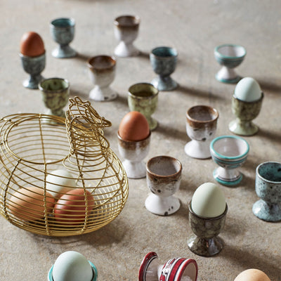 Various egg cups and a wire basket with eggs on a textured surface